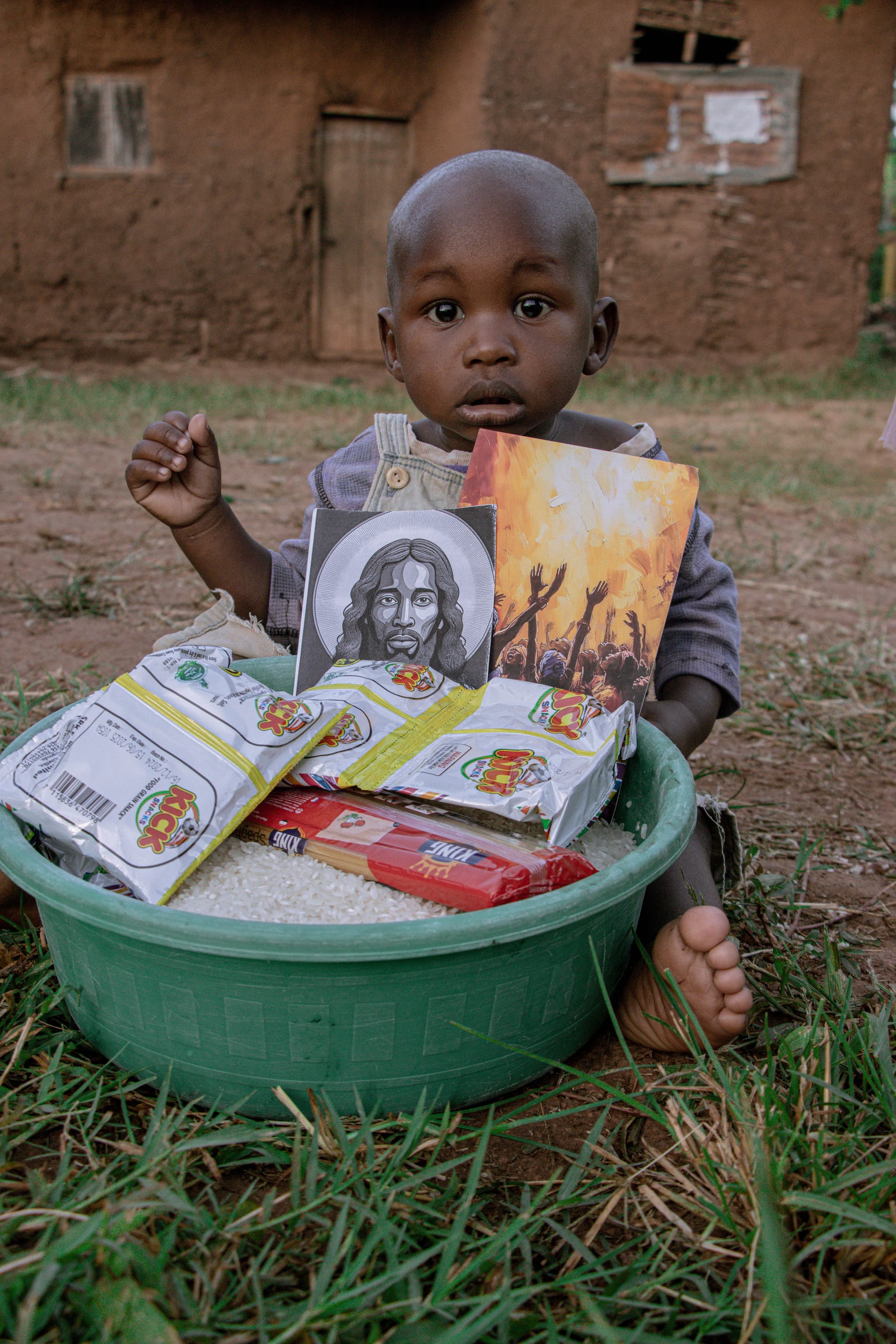 Young child seated outdoors with a green bowl of food gift packets and a gospel tract.