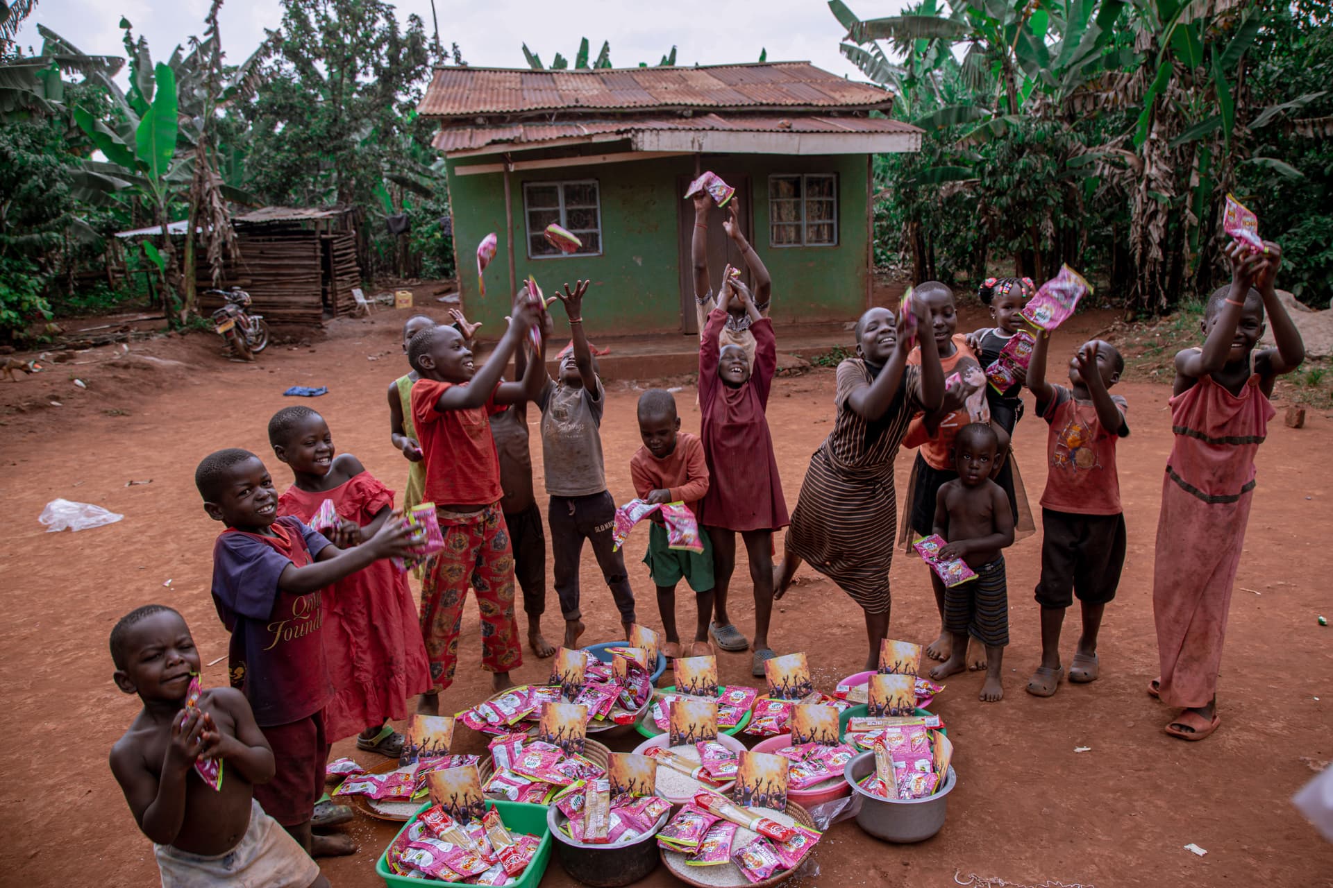Group of villagers, including children, gathered around baskets of food on the ground, one person raising food overhead.