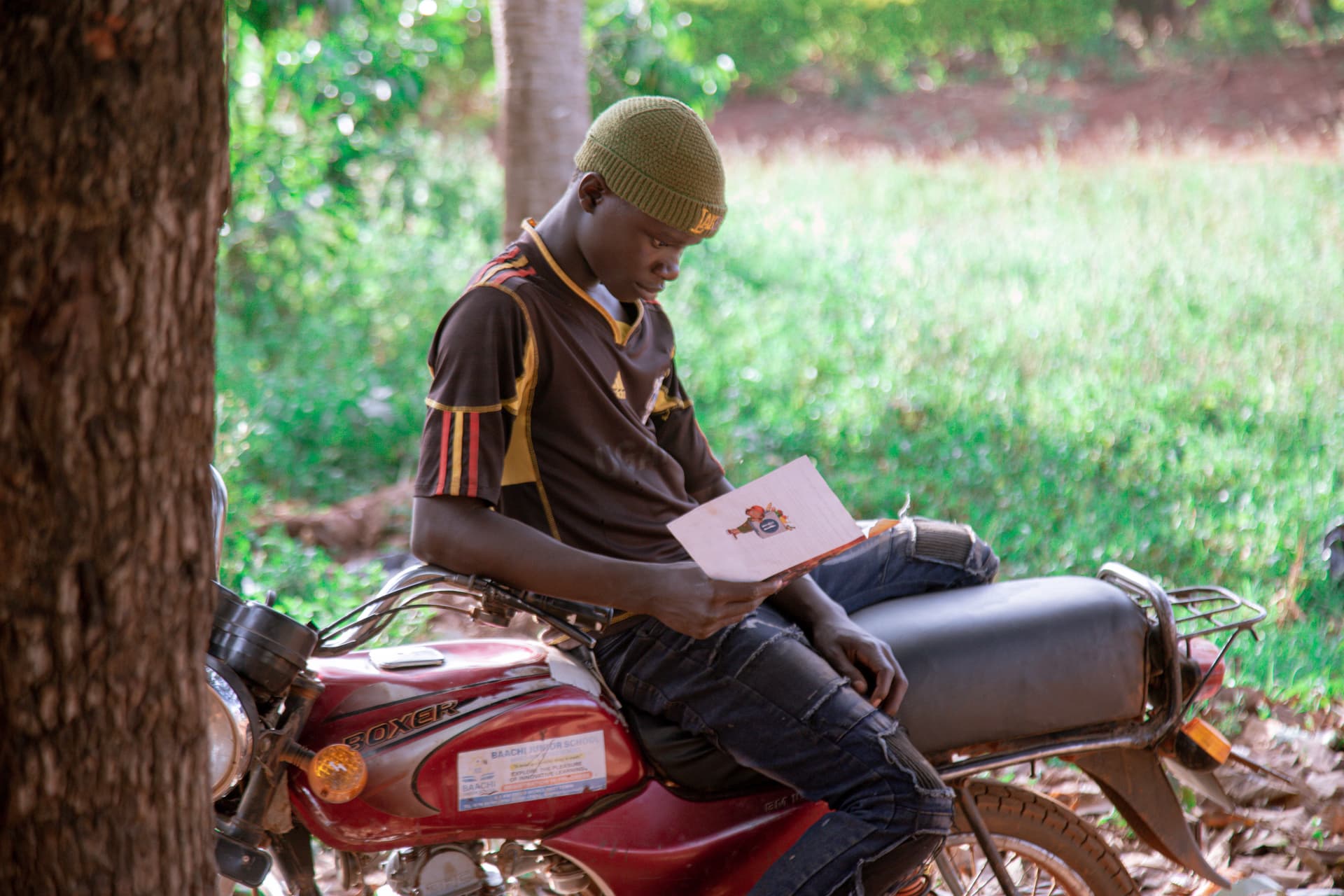 Man riding a motorcycle boda-boda while reading a document.