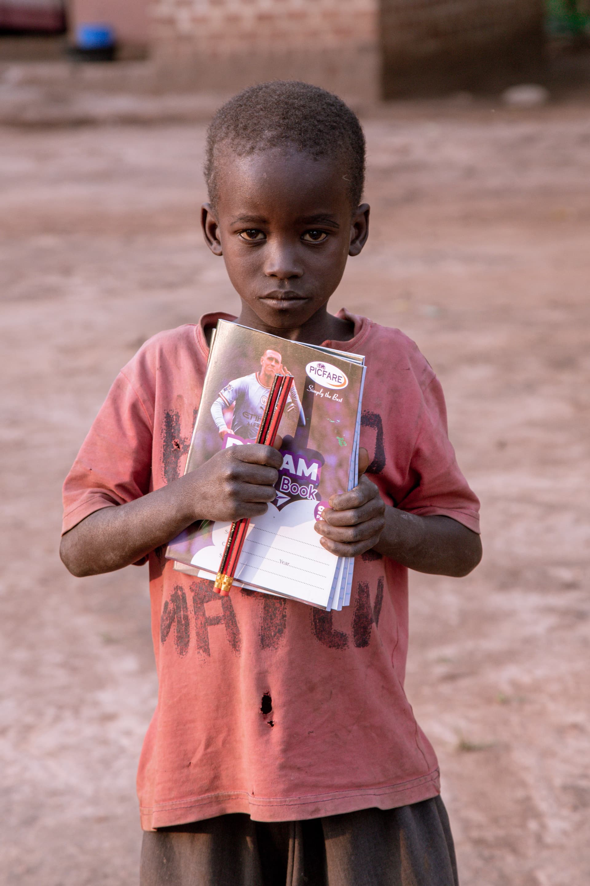 Boy standing outdoors in an orange shirt, holding up a booklet or leaflet.