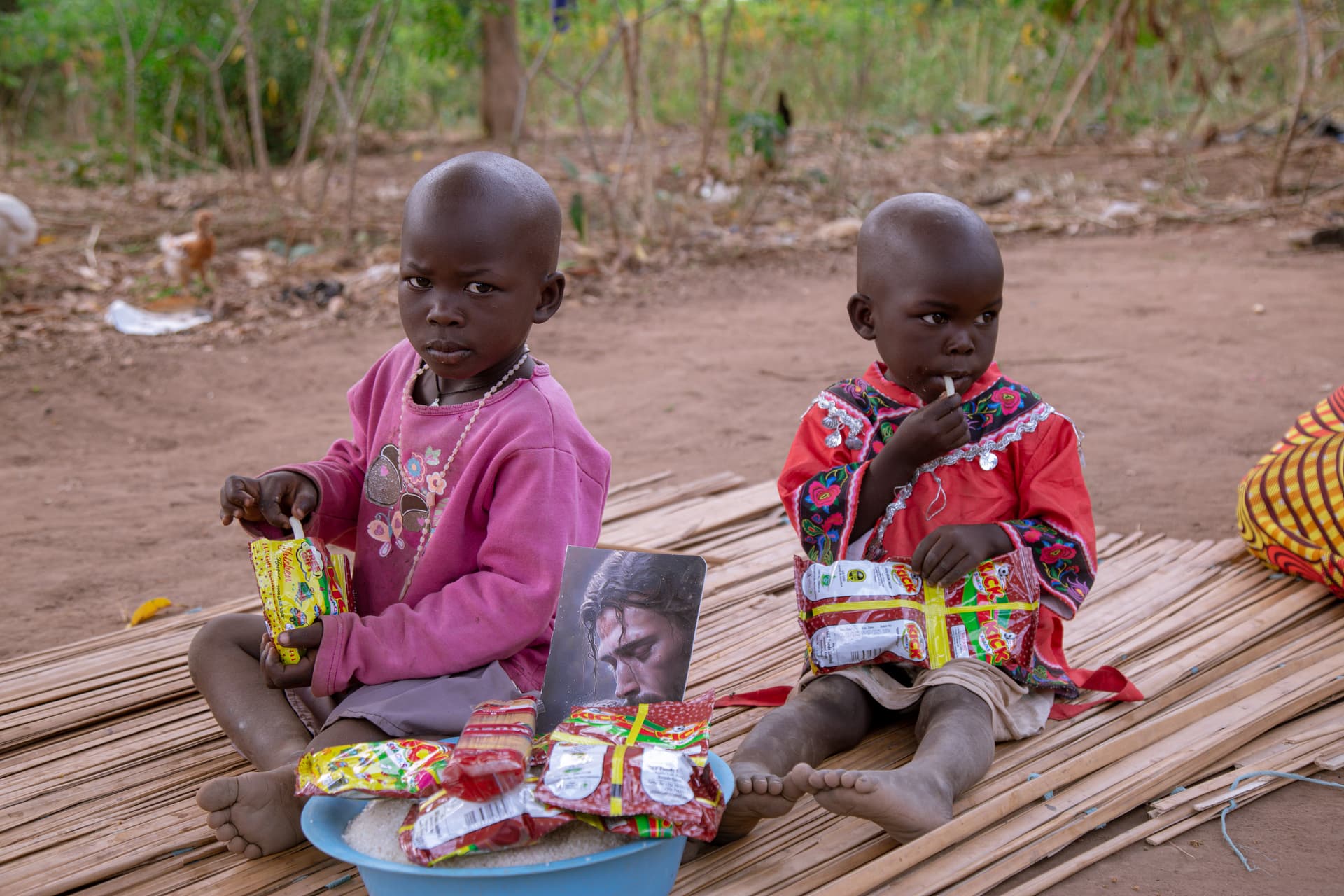 Two children sit together holding a printed photo card and a packaged food item.