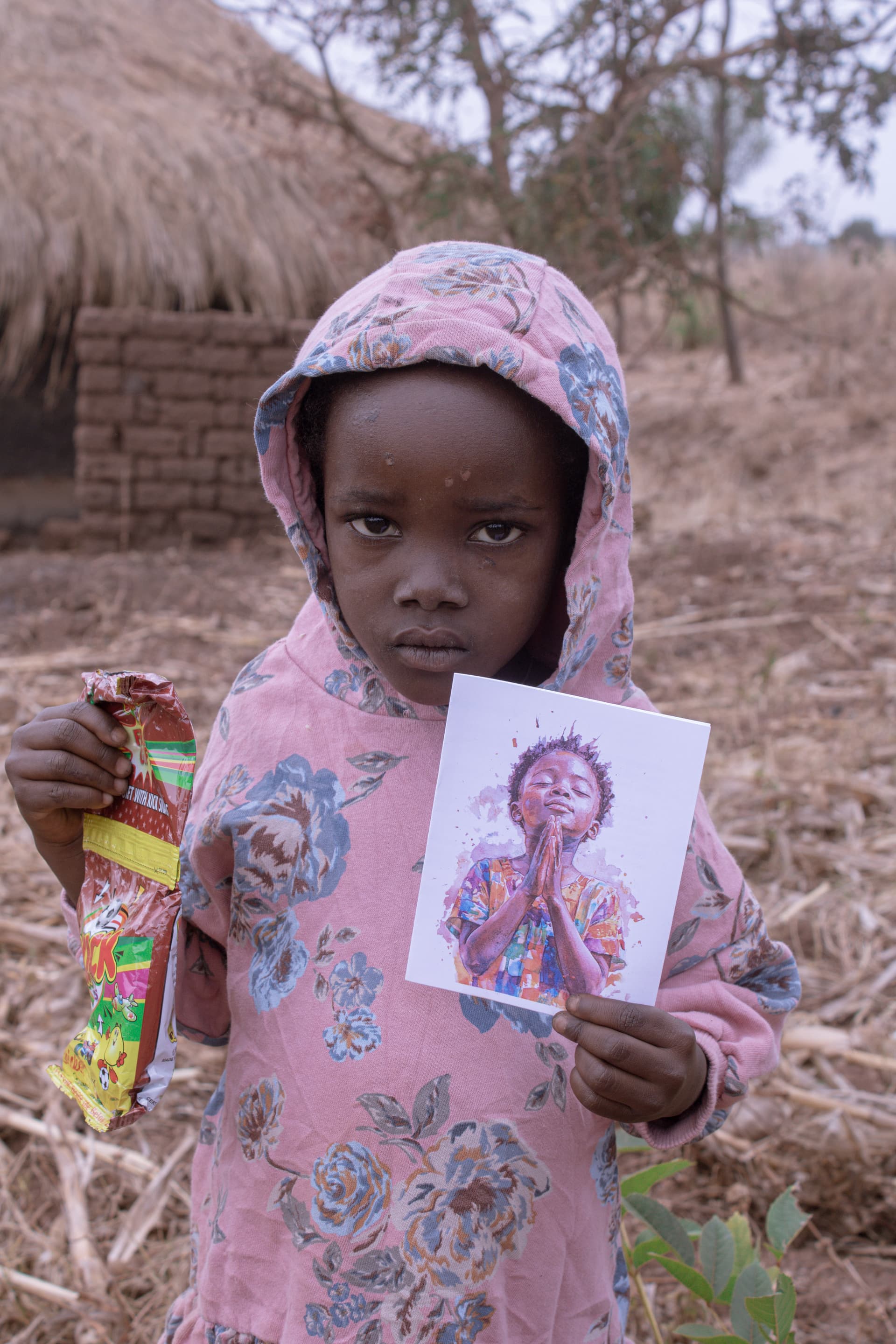 Esther, a young deaf girl in a pink headscarf, holds a devotional card and small food package.