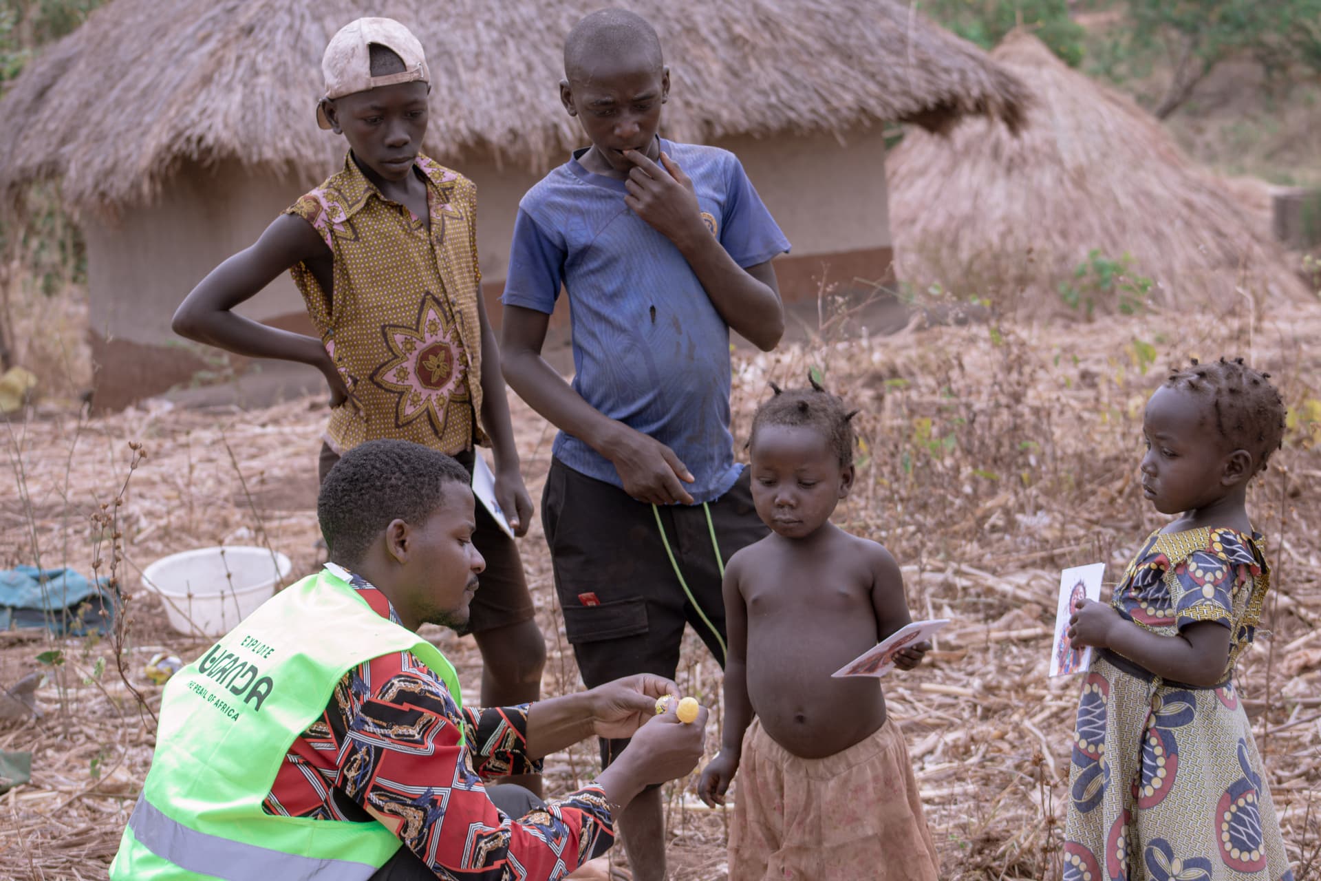 JFM team members measure a child's arm outside thatched-roof huts during a village visit.