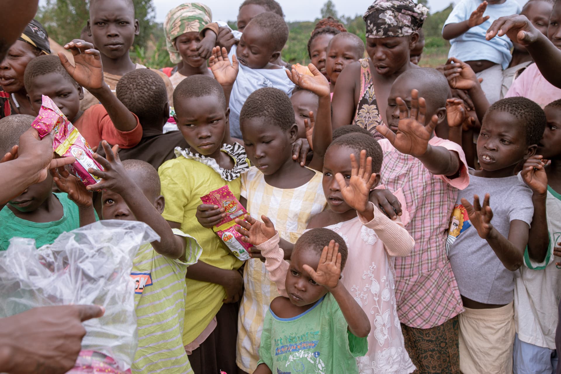 Group of children reaching their hands up toward the camera, receiving items during distribution.