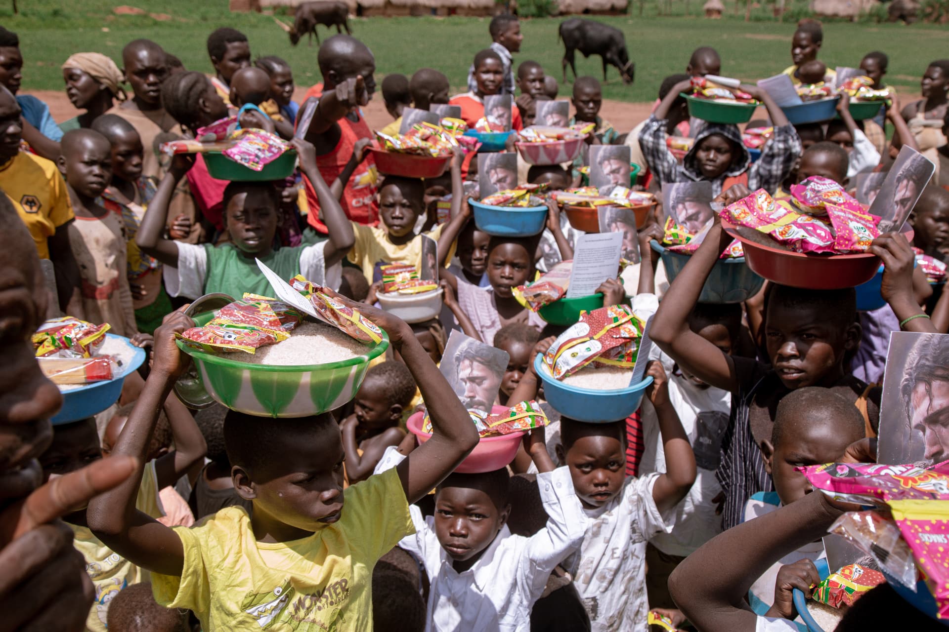 Large crowd of village children carrying food baskets and bowls balanced on their heads.
