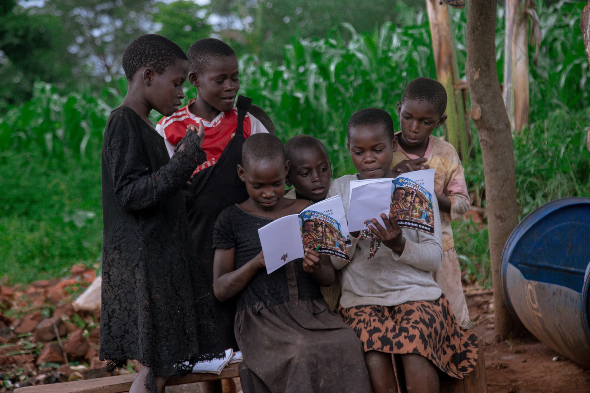 A group of children read a gospel tract together outdoors near a mud house.
