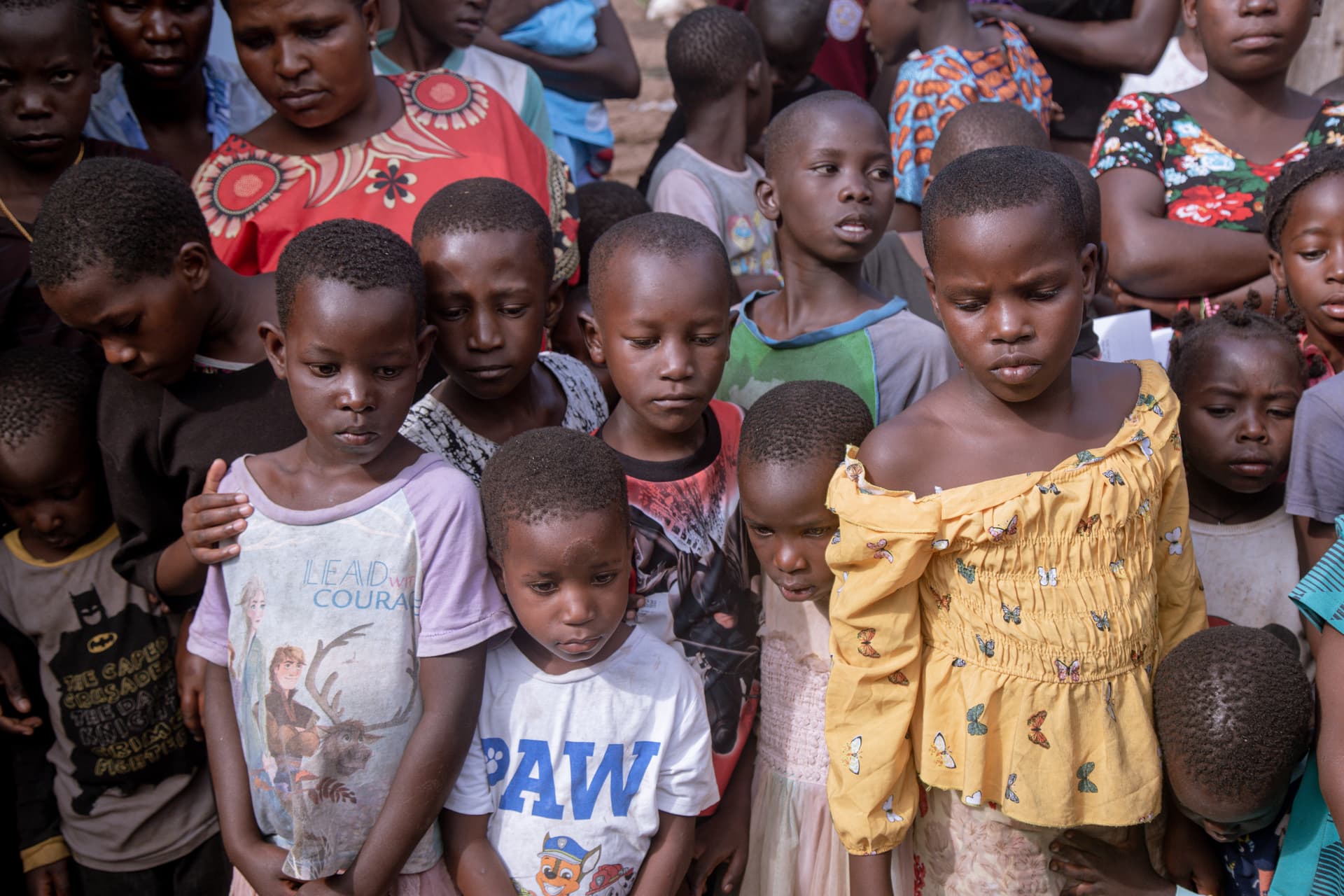 A group of children in colorful shirts stand close together outdoors.