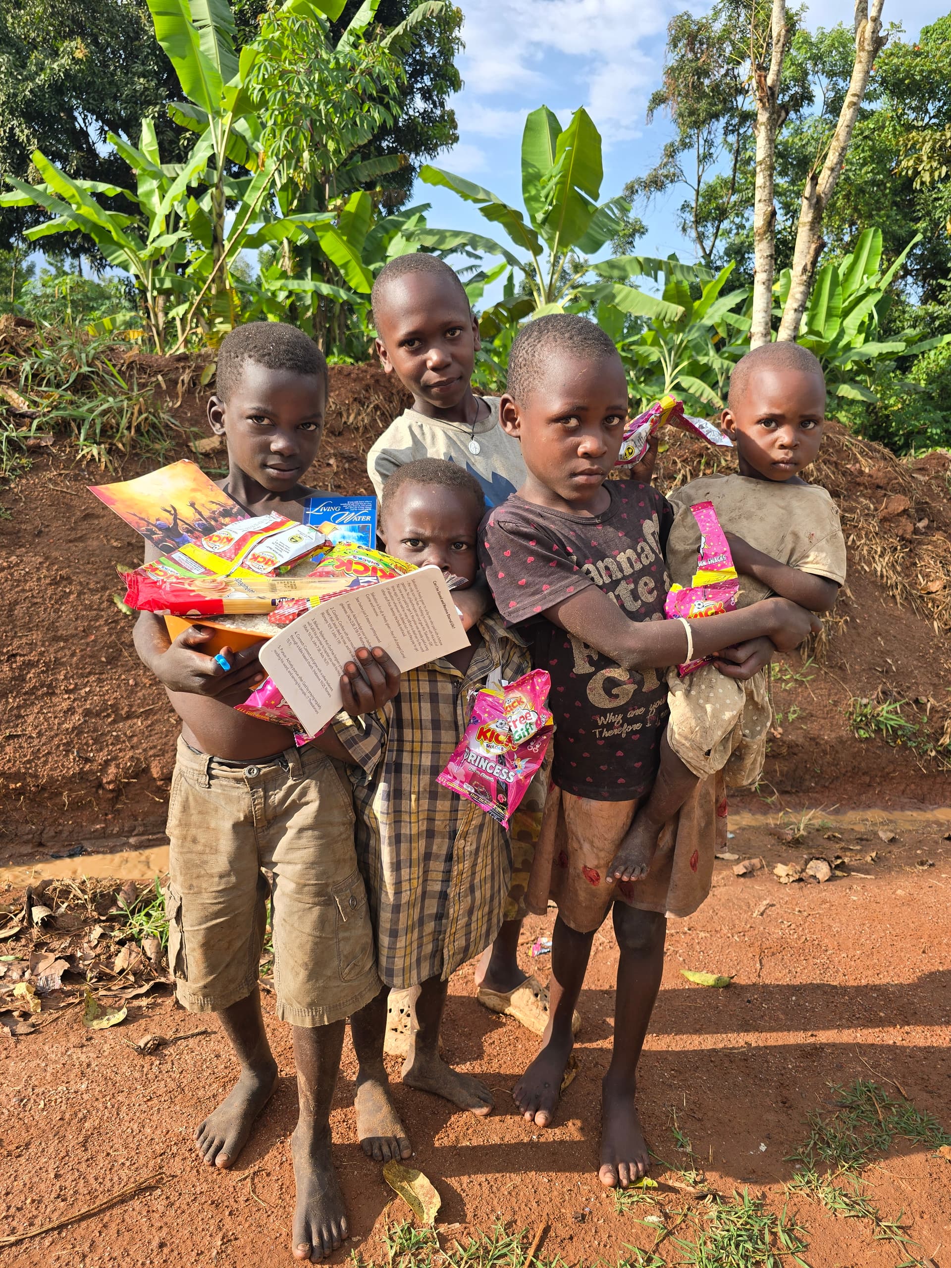 Children outdoors hold bags of snacks and a branded grocery box given as a food gift.