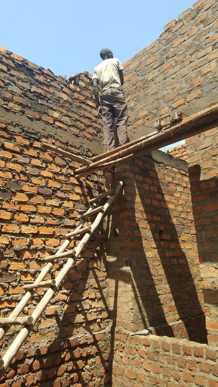 A worker stands on wooden scaffolding atop an unfinished brick wall at the CVTI Institute construction site.