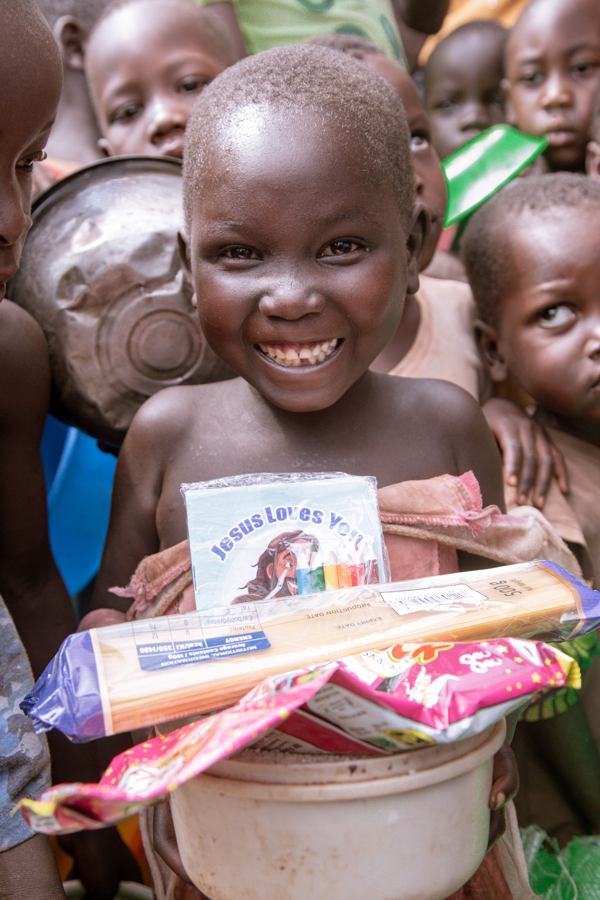 Several children holding long spaghetti-style food packets in colorful wrapping, smiling.