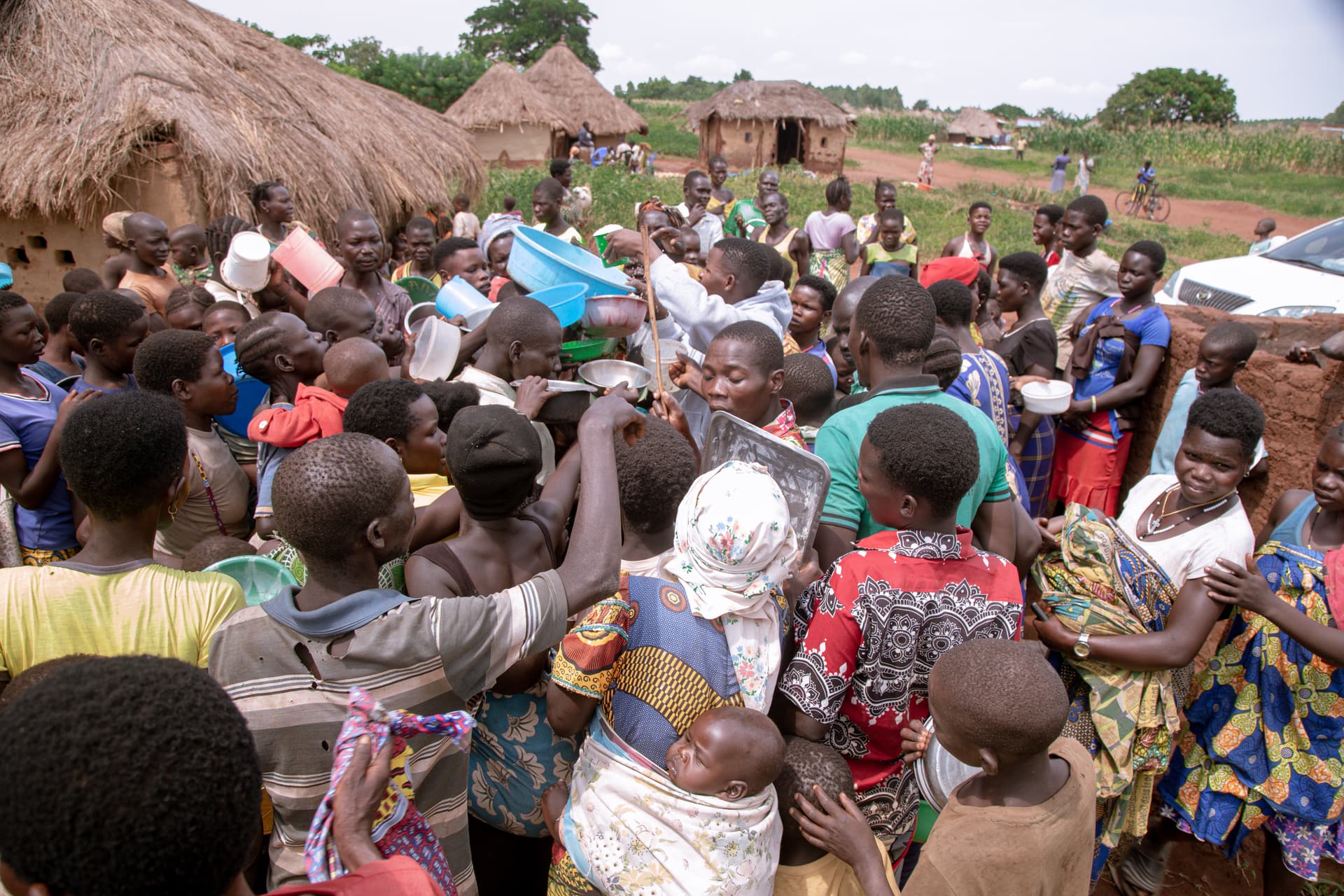 Crowd of women and children gathered outdoors with hands raised during a food distribution.
