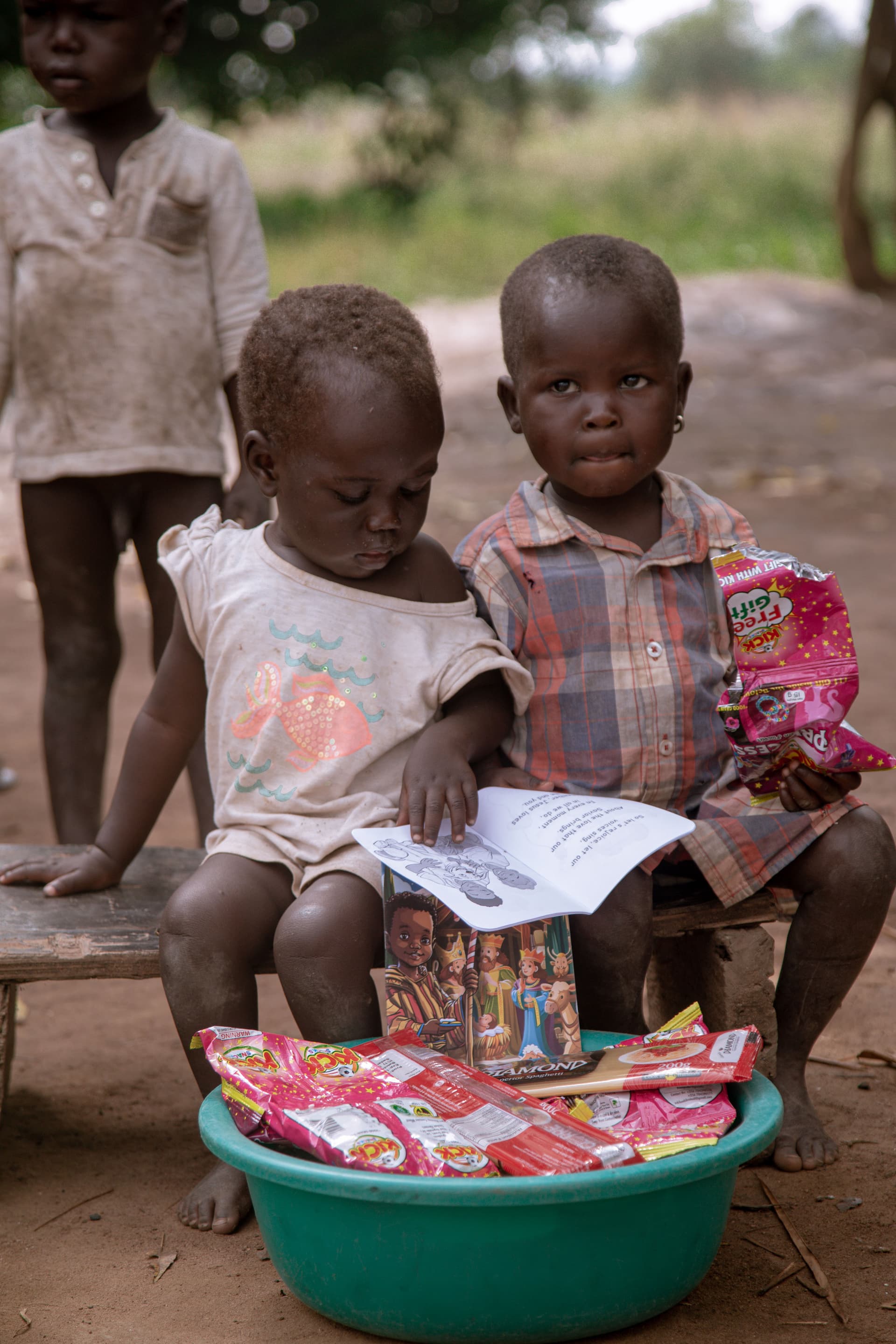 Two children sitting on a green basin of food packets while reading a pamphlet together.