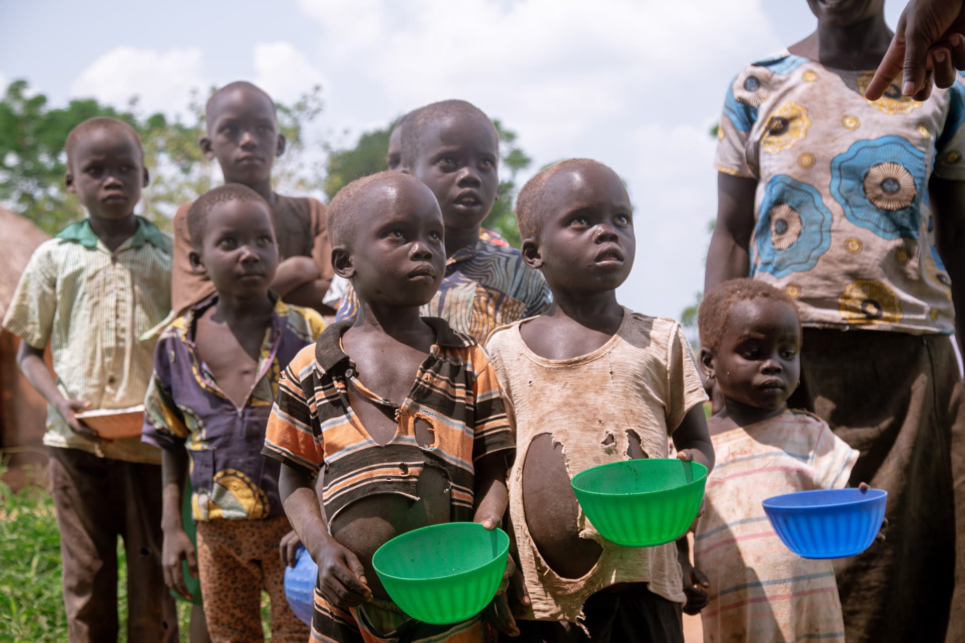 Line of children reaching for green and blue bowls being handed out during a food outreach.