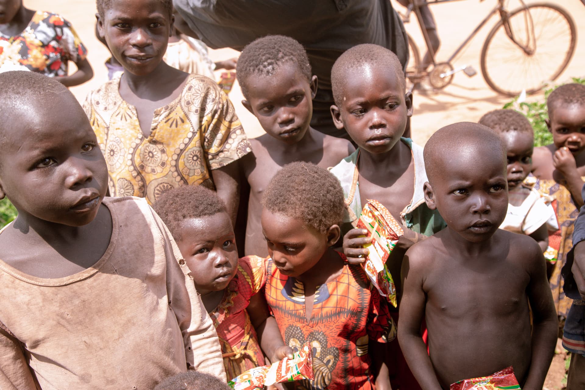 Group of thin children standing together outdoors near a bicycle in the Isunga/Ogwal area of northern Uganda.