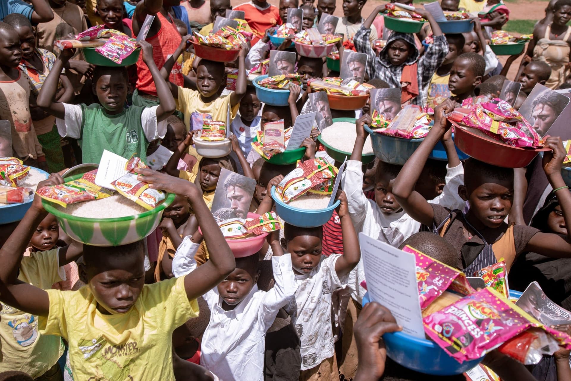 A crowd of children carry packaged food gift bundles on their heads at a JFM distribution event.