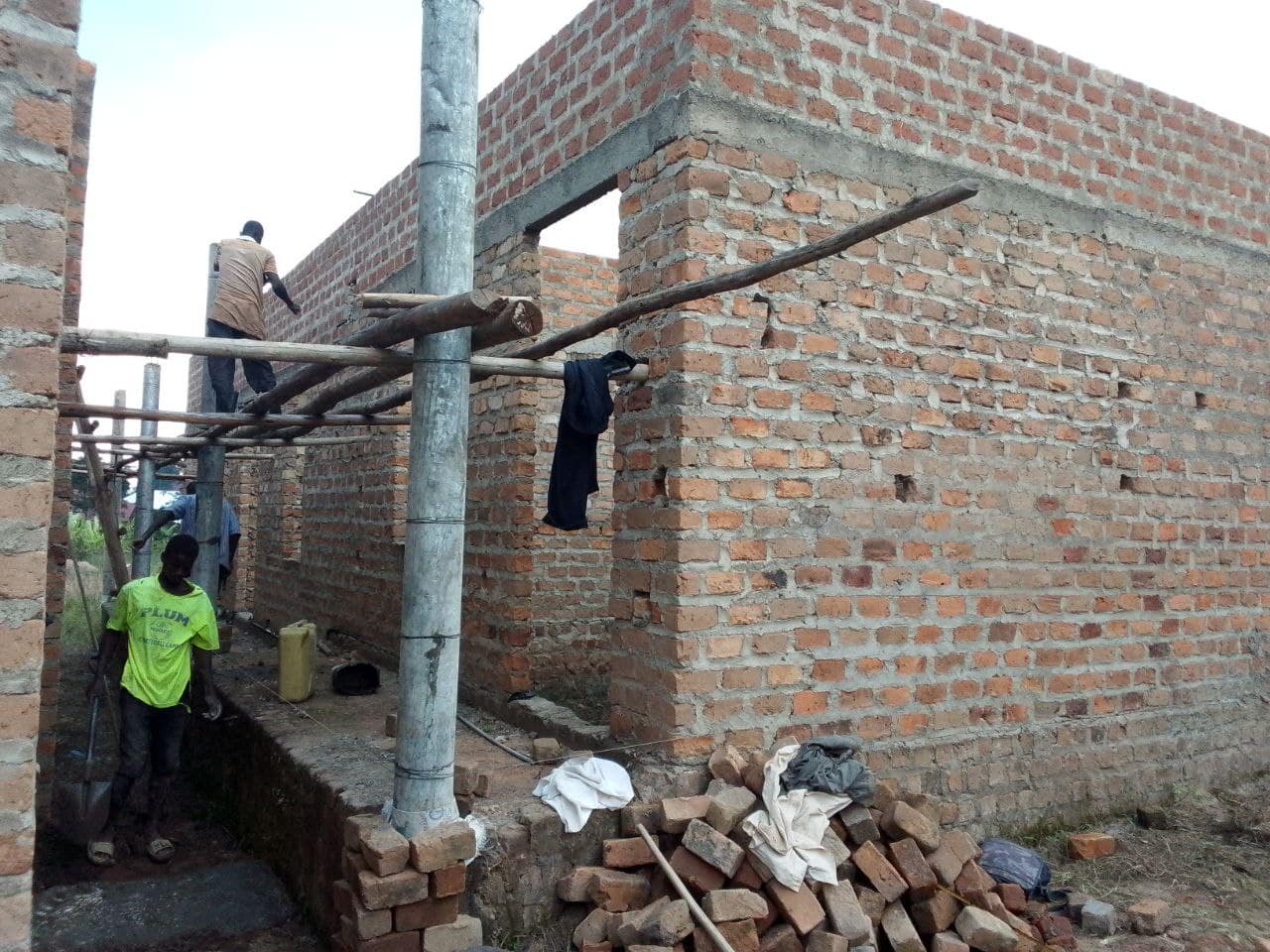A partially built brick building at CVTI Institute with a worker on scaffolding near a roof support pole.