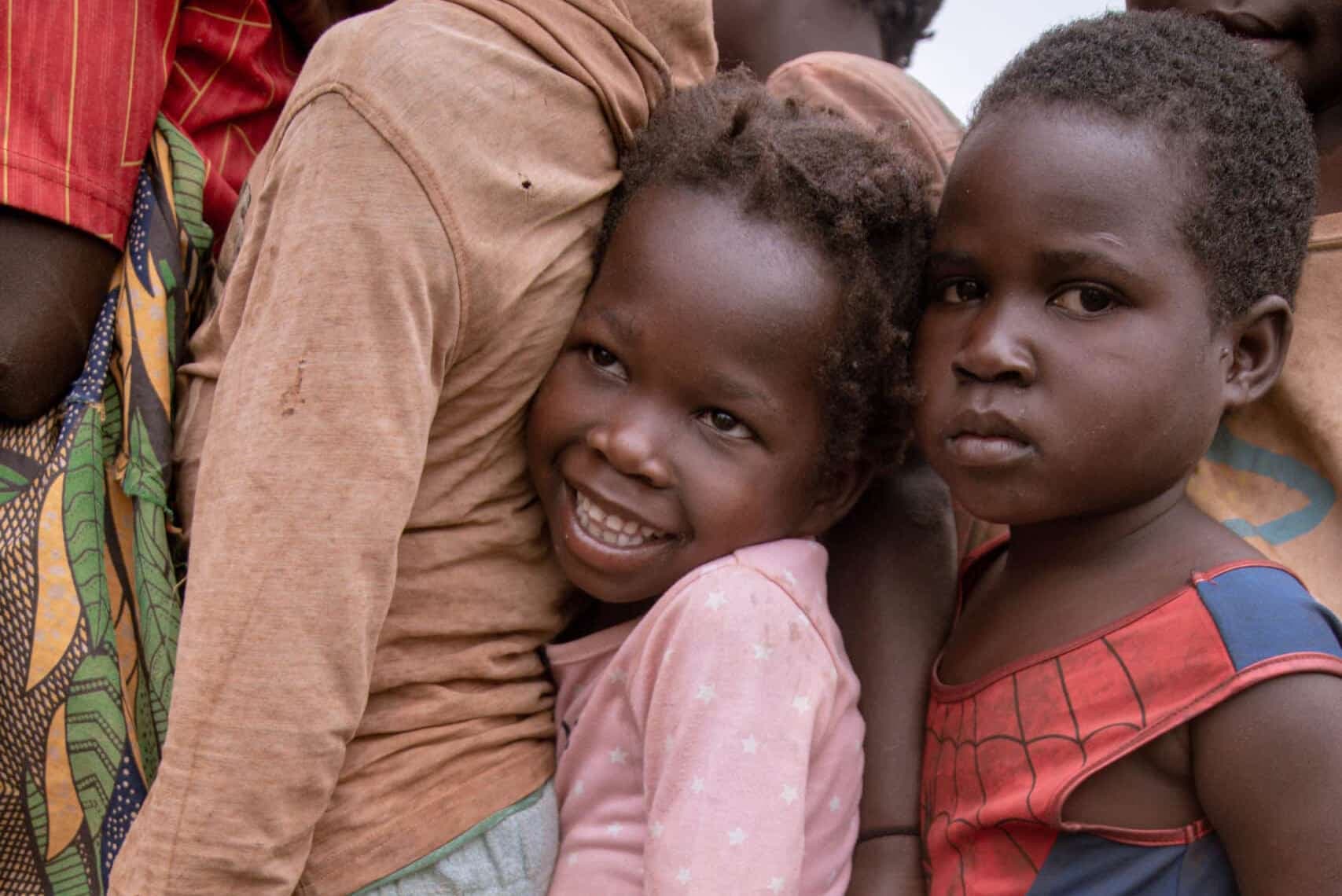 Three young children stand close together outdoors, one resting a hand on another's shoulder.