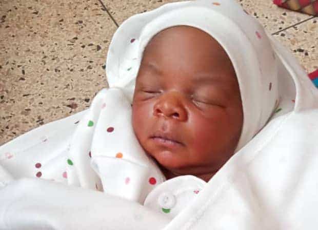 A newborn baby wrapped in a white polka-dot blanket and cap sleeps peacefully.