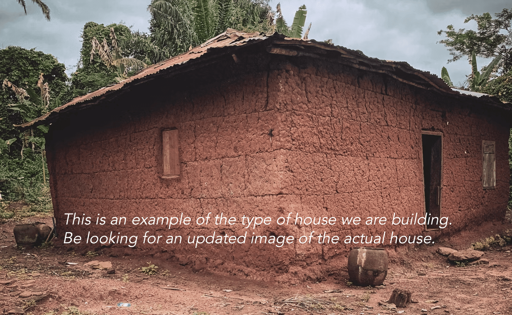 Small mud-walled house with a thatched roof, an example photo captioned as the type of house being built.