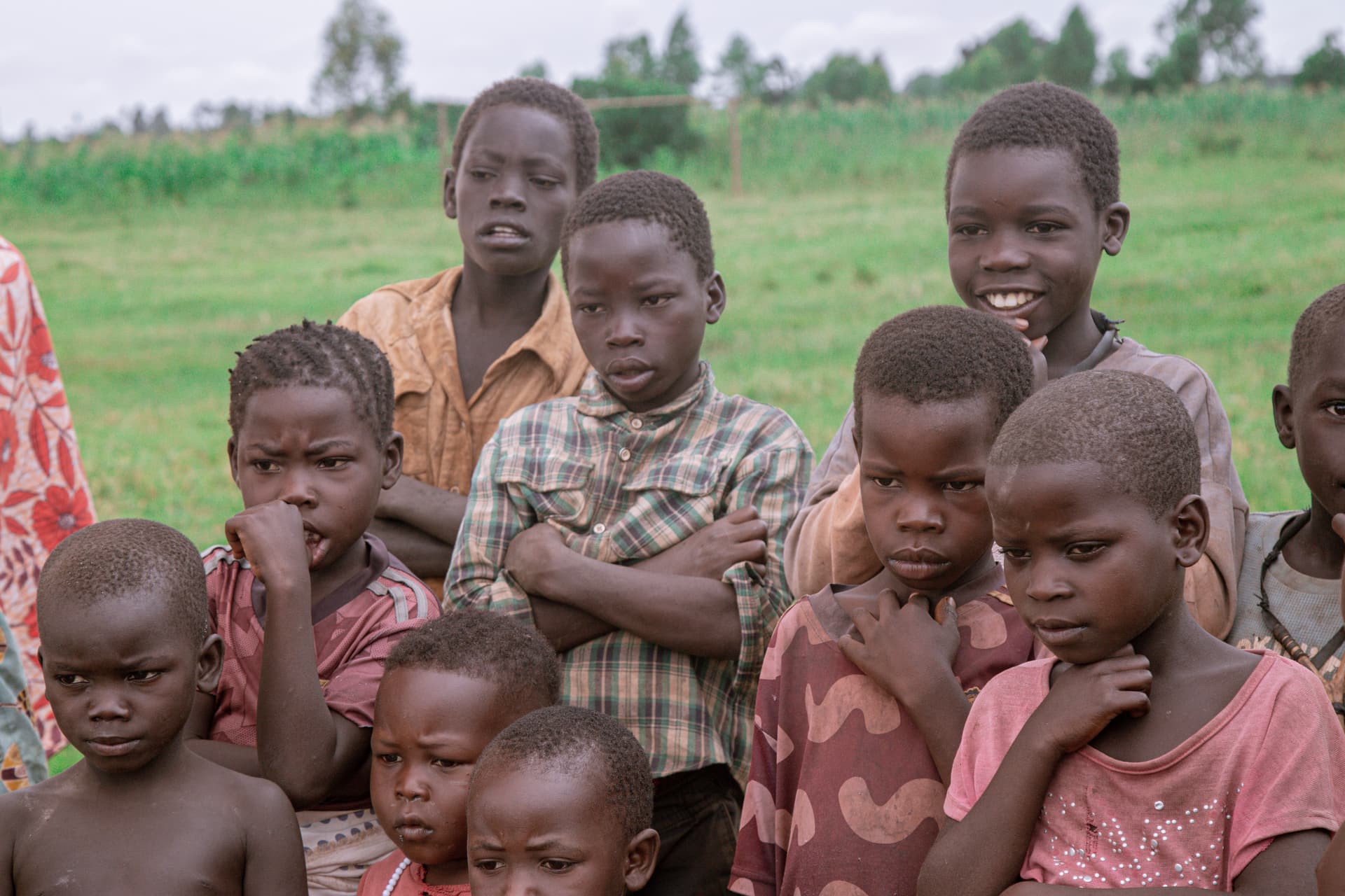 A group of children stand close together outdoors in an open green field.