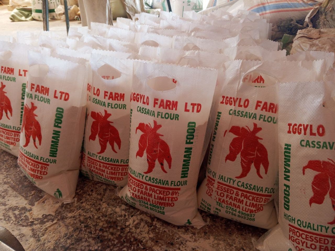 Stacked white sacks of Iggylo Farm Ltd cassava flour with a rooster logo are lined up for delivery.