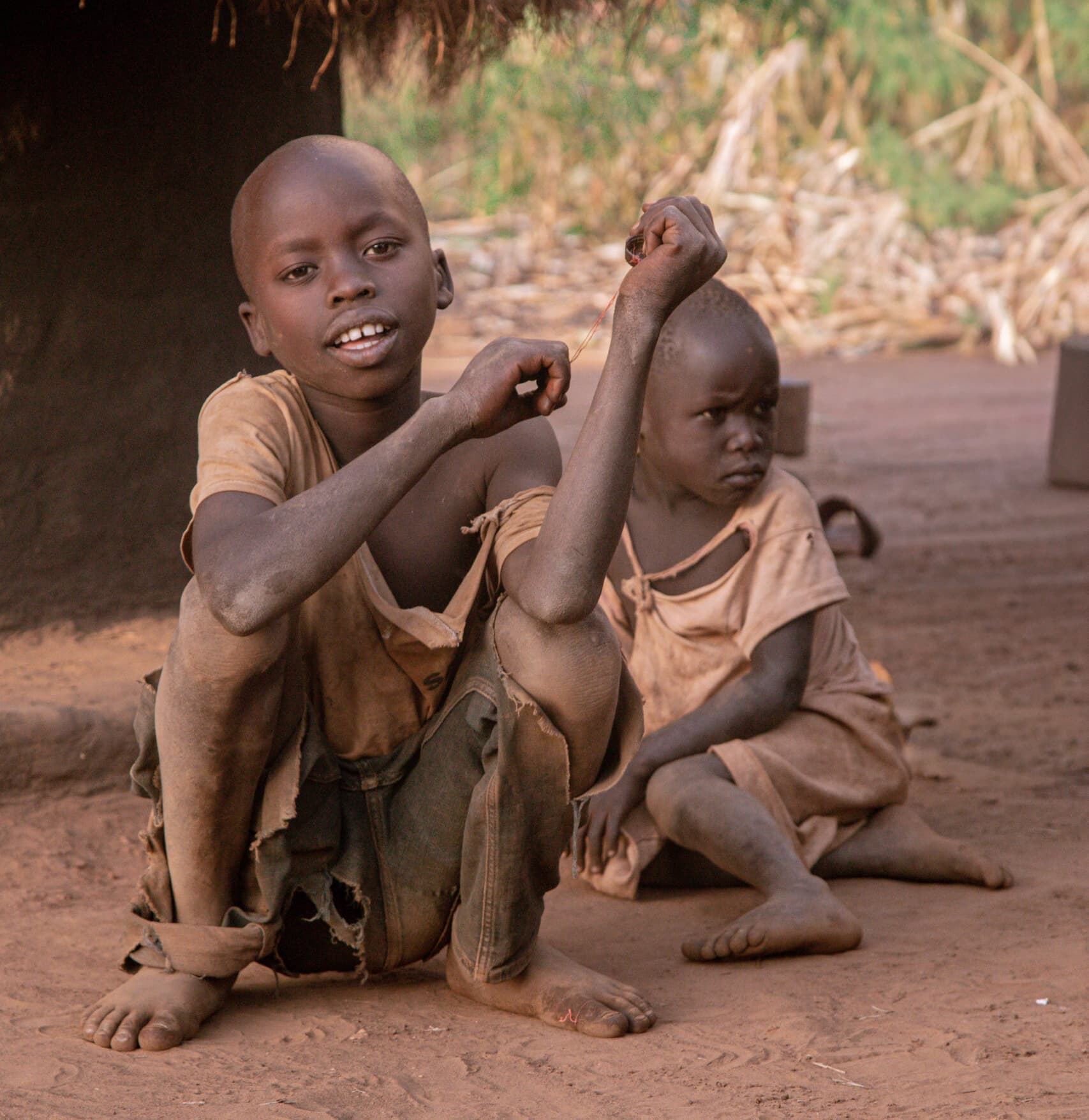 Vintage-toned photo of two young children sitting together on bare dirt ground.