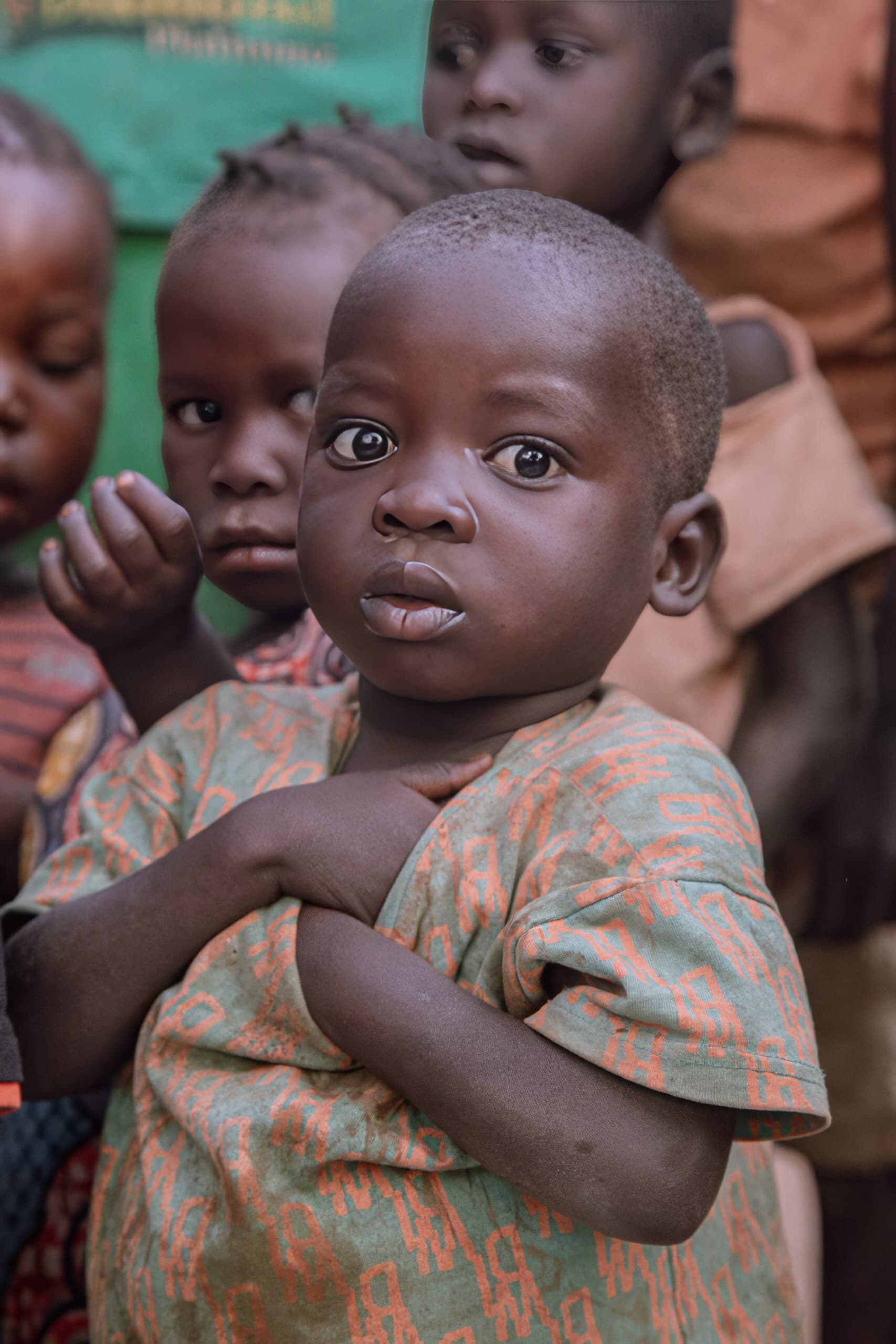 Two children embrace closely, one wearing a colorful patterned dress.