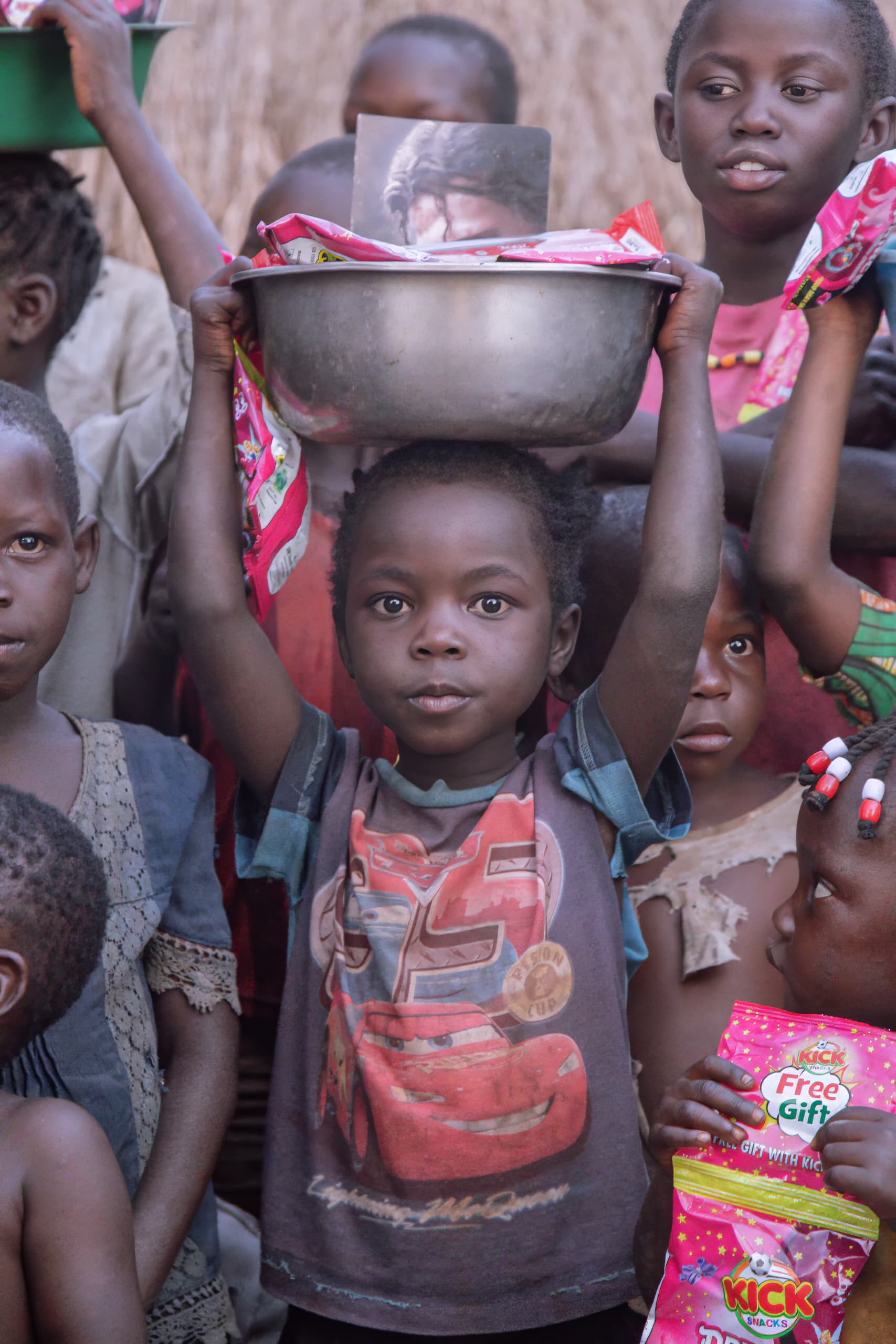 A child carries a basin of food packets on his head while other children look on.
