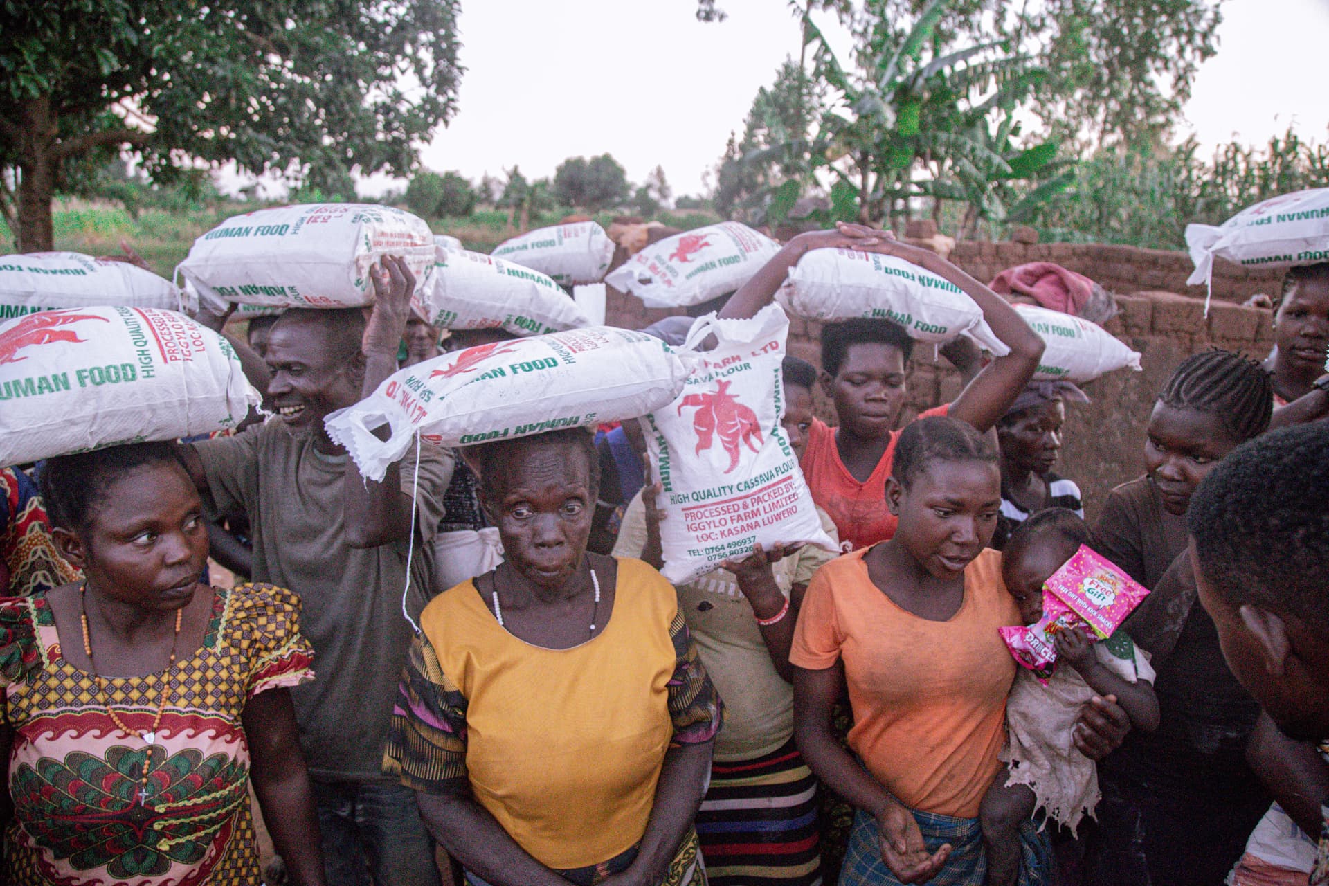 Group of women carry sacks of food on their heads along an outdoor path.