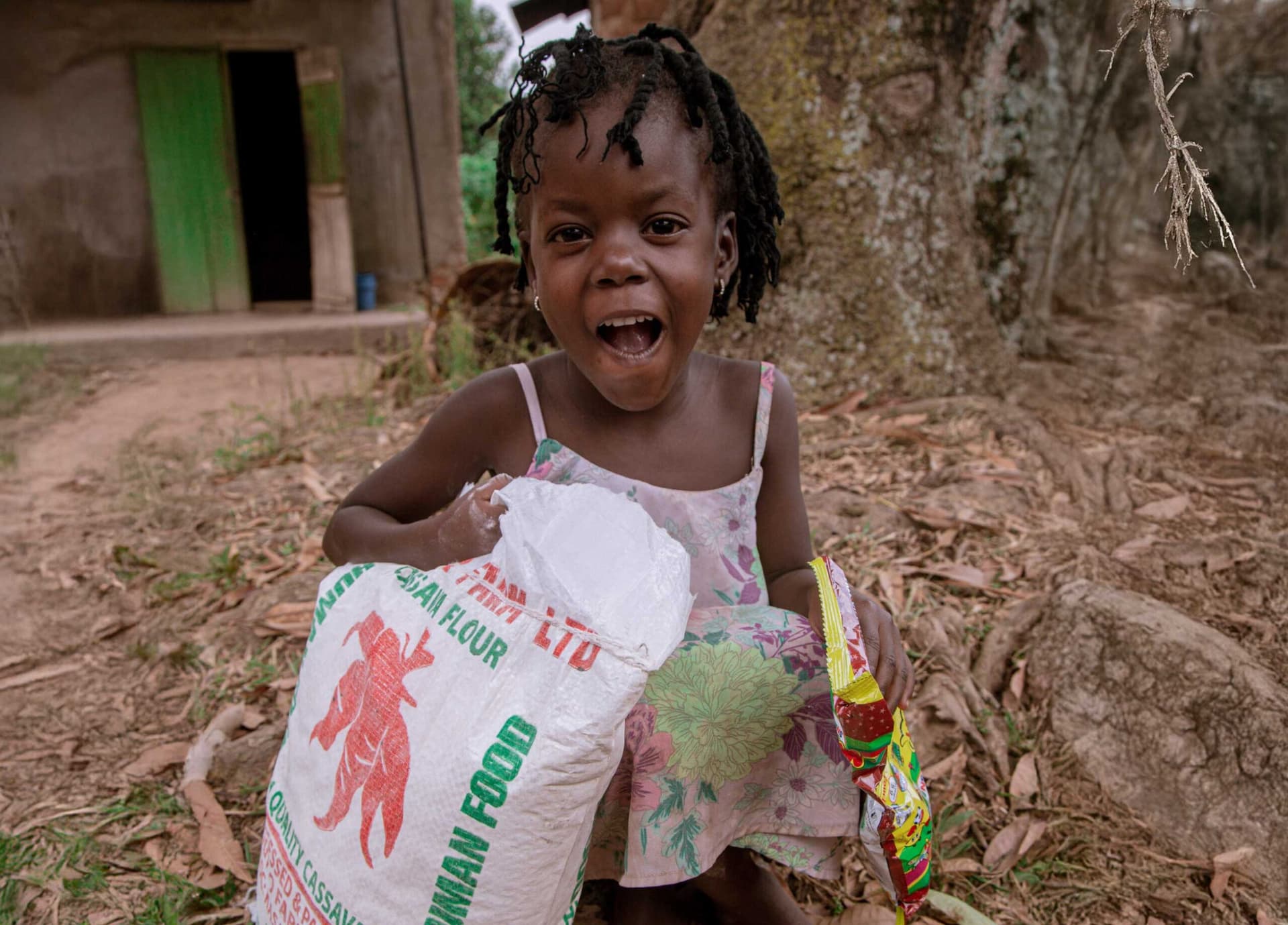 A young girl laughs while holding a bag of cassava flour and a bundle of greens.
