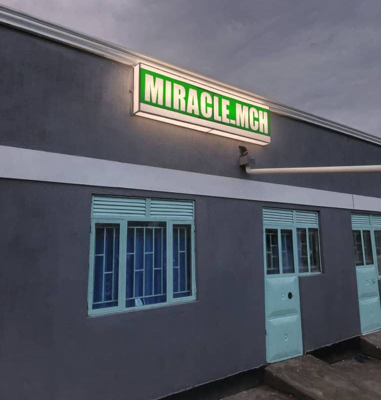 Illuminated green MIRACLE MCH sign mounted on the exterior wall of the clinic building at night.