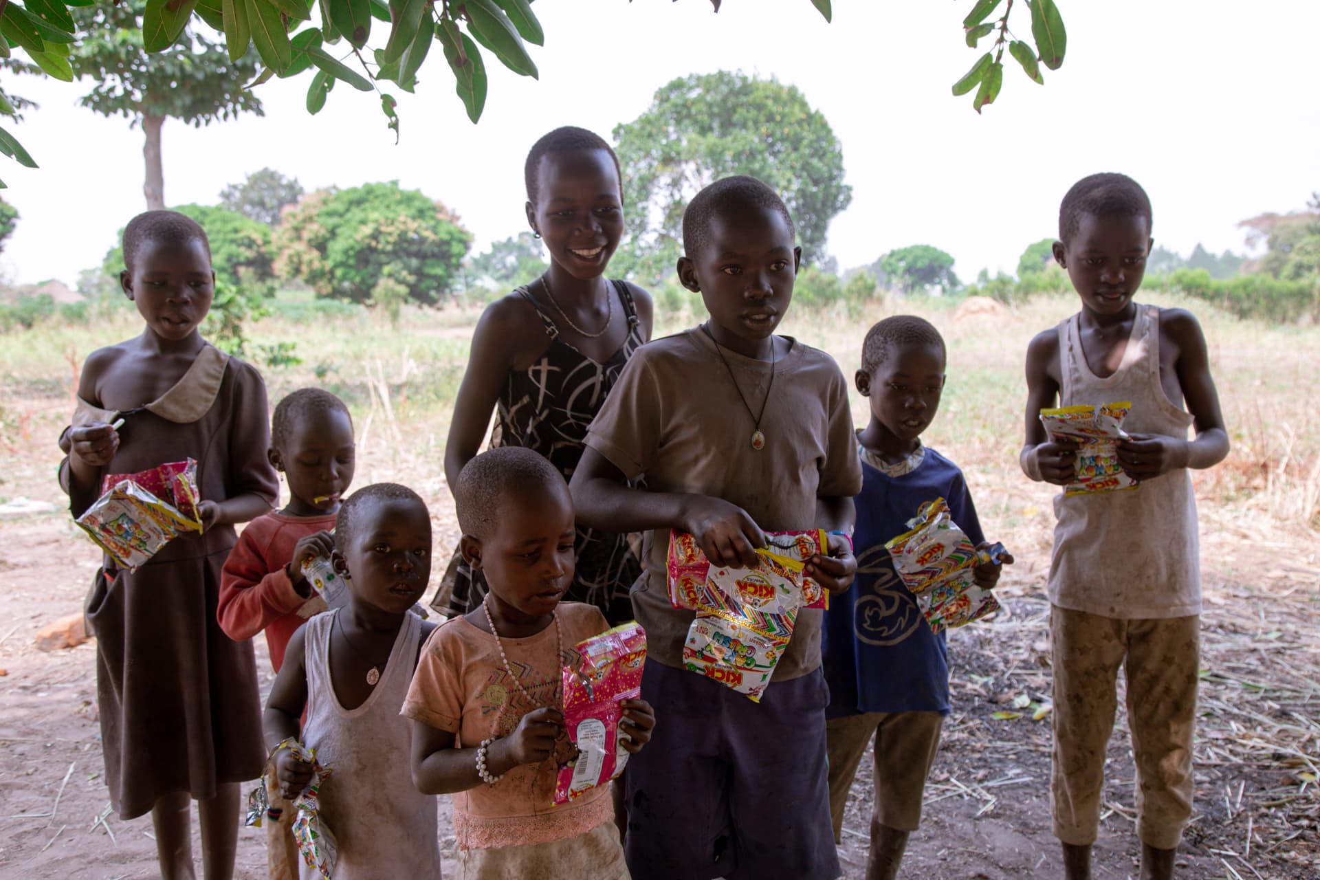 Group of children standing on a dirt path holding food packages they received.
