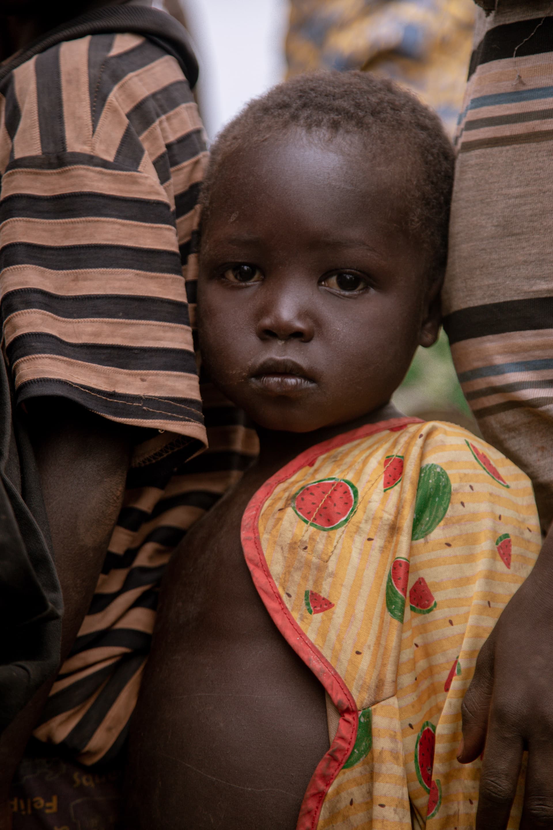 Young child in a single patterned wrap being carried on someone's back.