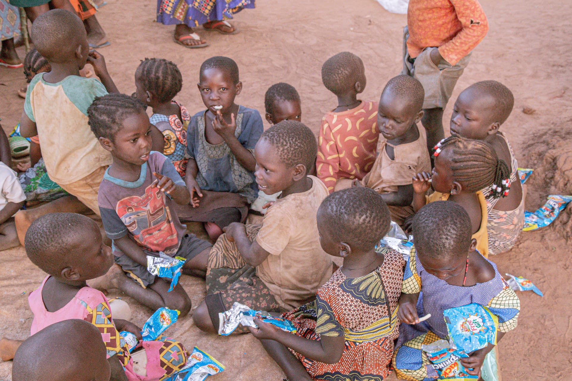 Group of children seated closely together on a mat outdoors, listening attentively.