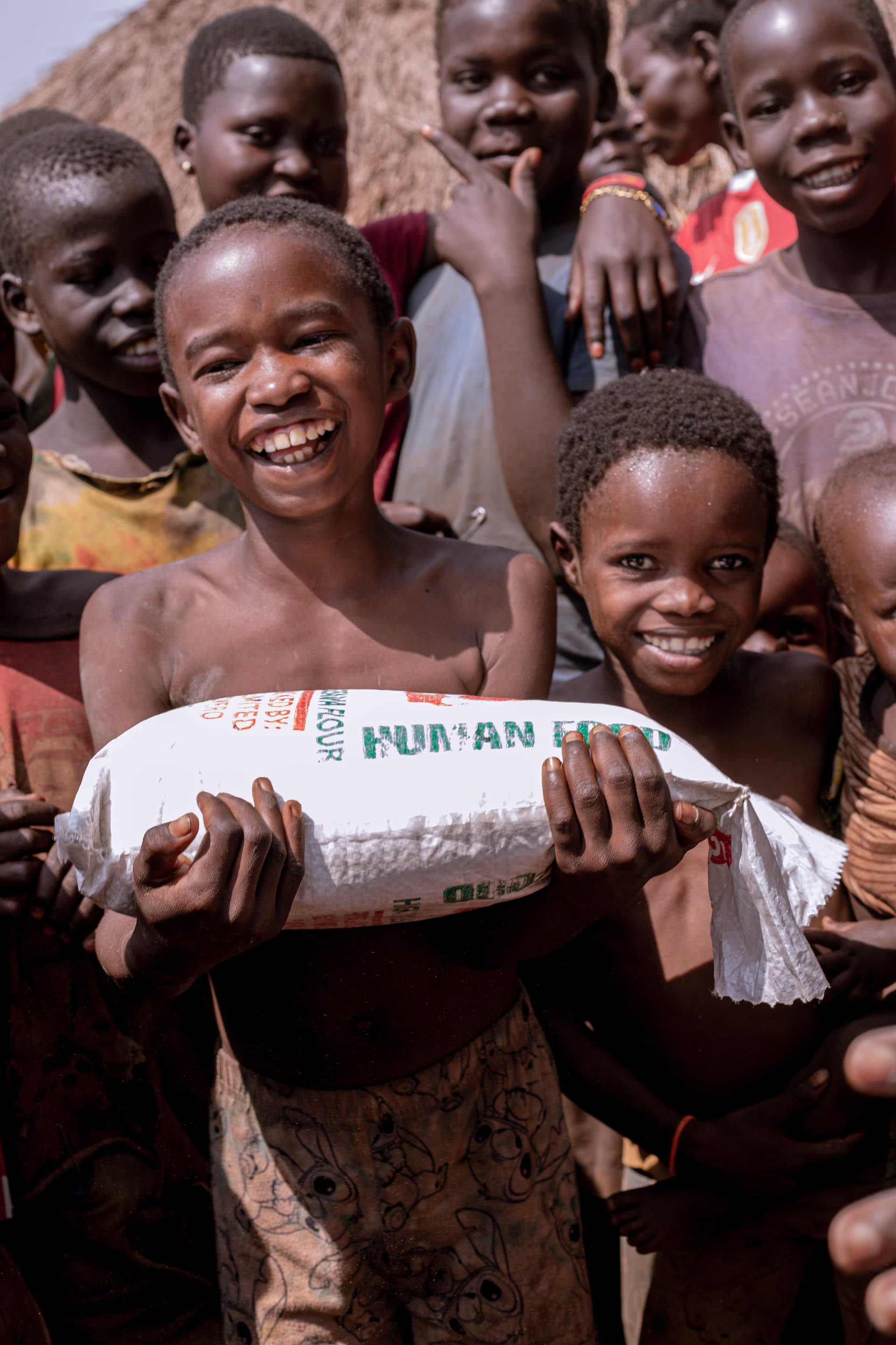 Smiling girl holding a bag of rice while surrounded by other children outdoors.