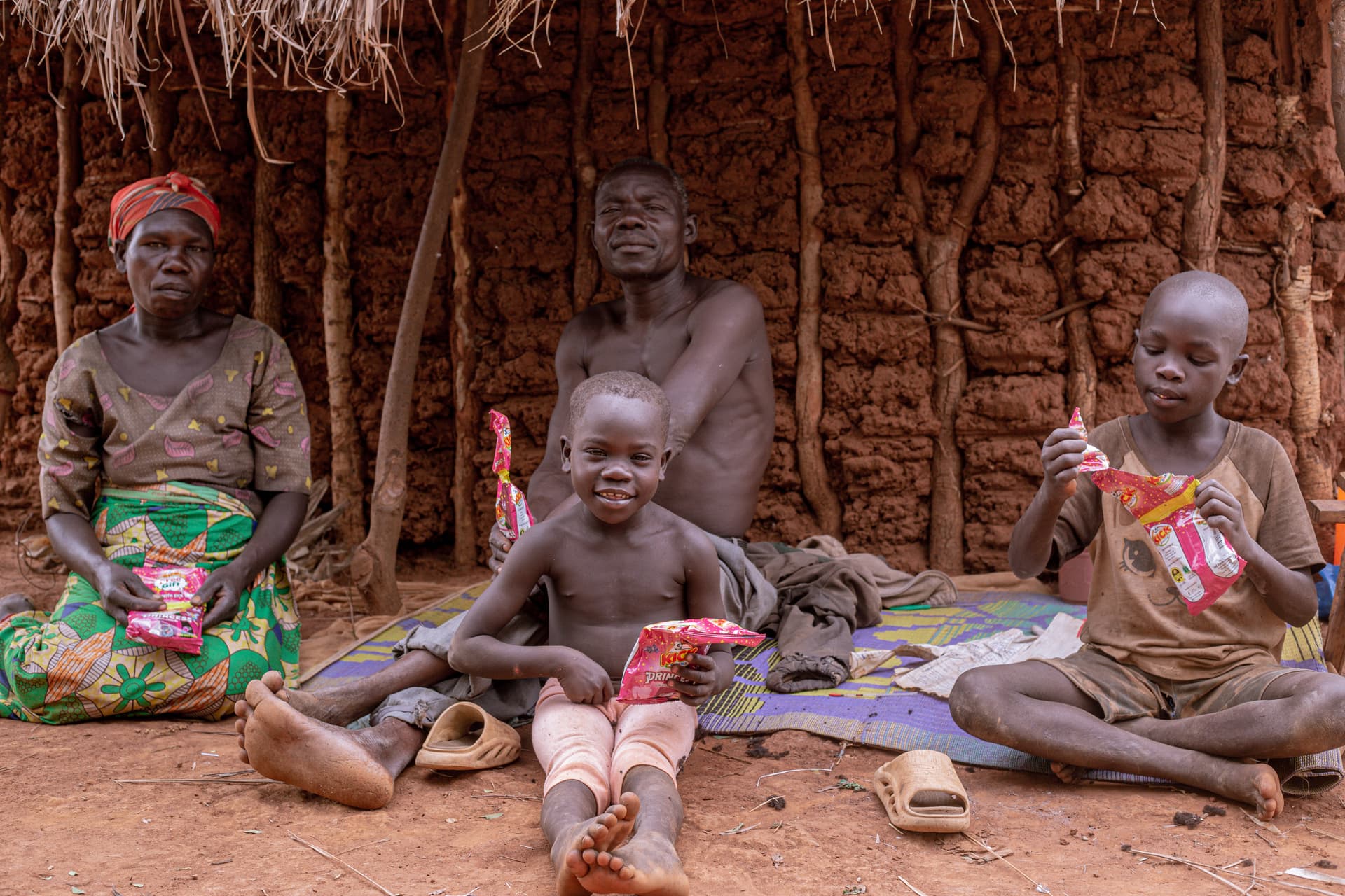 Father and mother sit with their children outside a mud-brick hut.