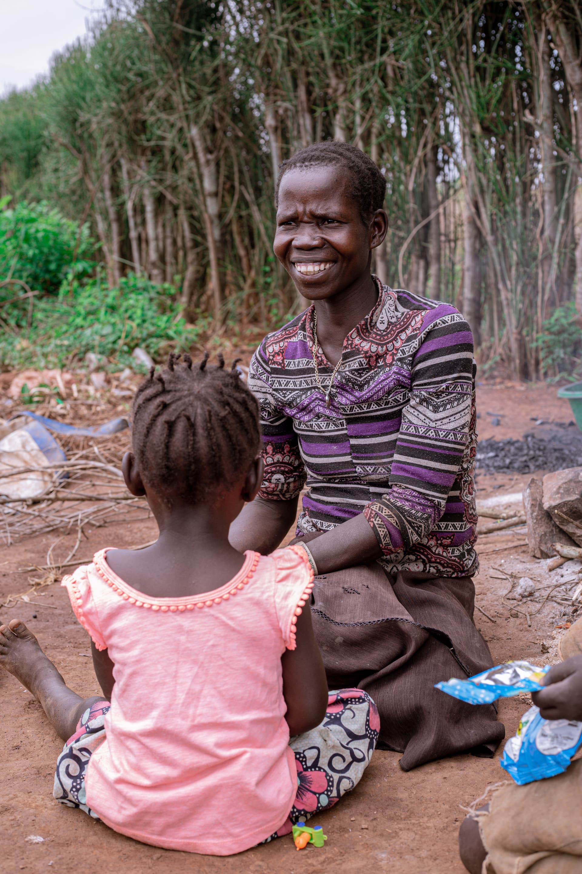 Elderly woman sits with a young girl in a pink dress, both smiling outdoors.