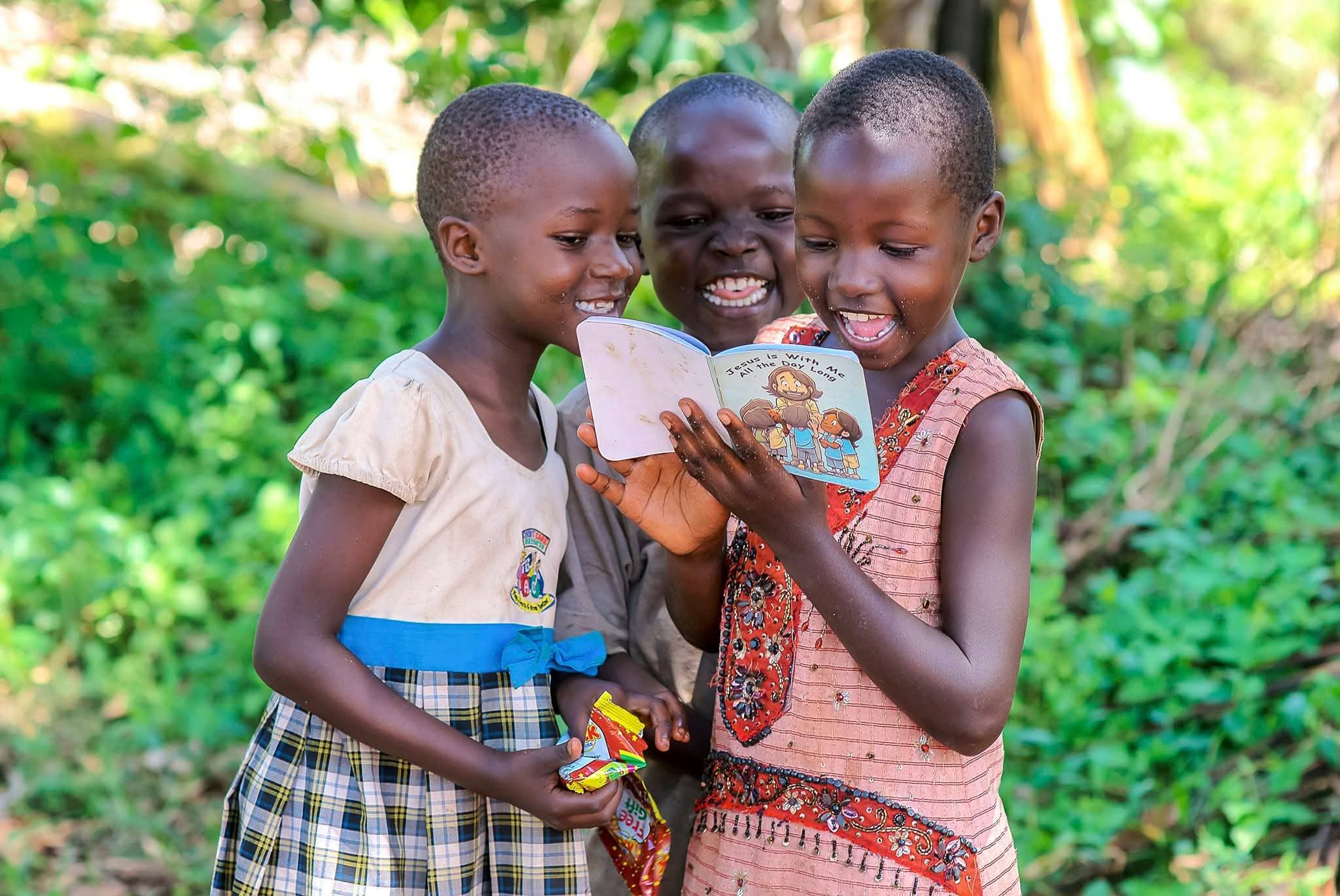Two young girls in dresses smile while one holds a picture book.
