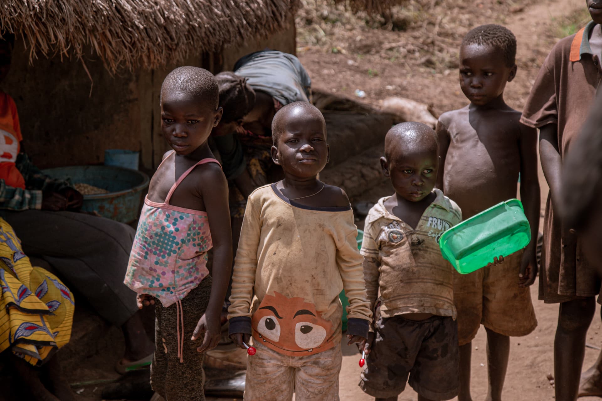 A group of young children standing together outdoors, one holding a green cloth item.