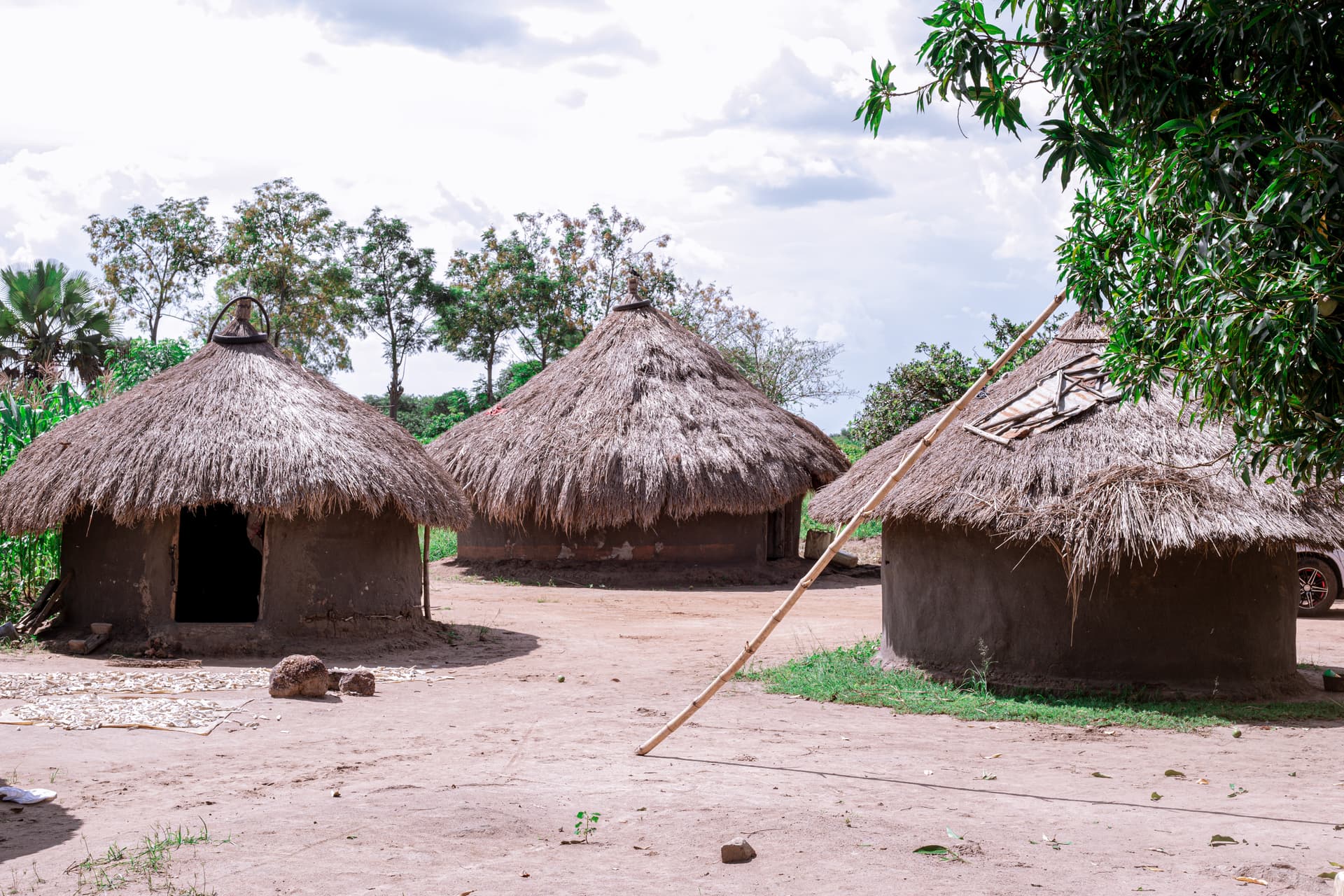 Three round thatched-roof mud huts clustered together under a cloudy sky.