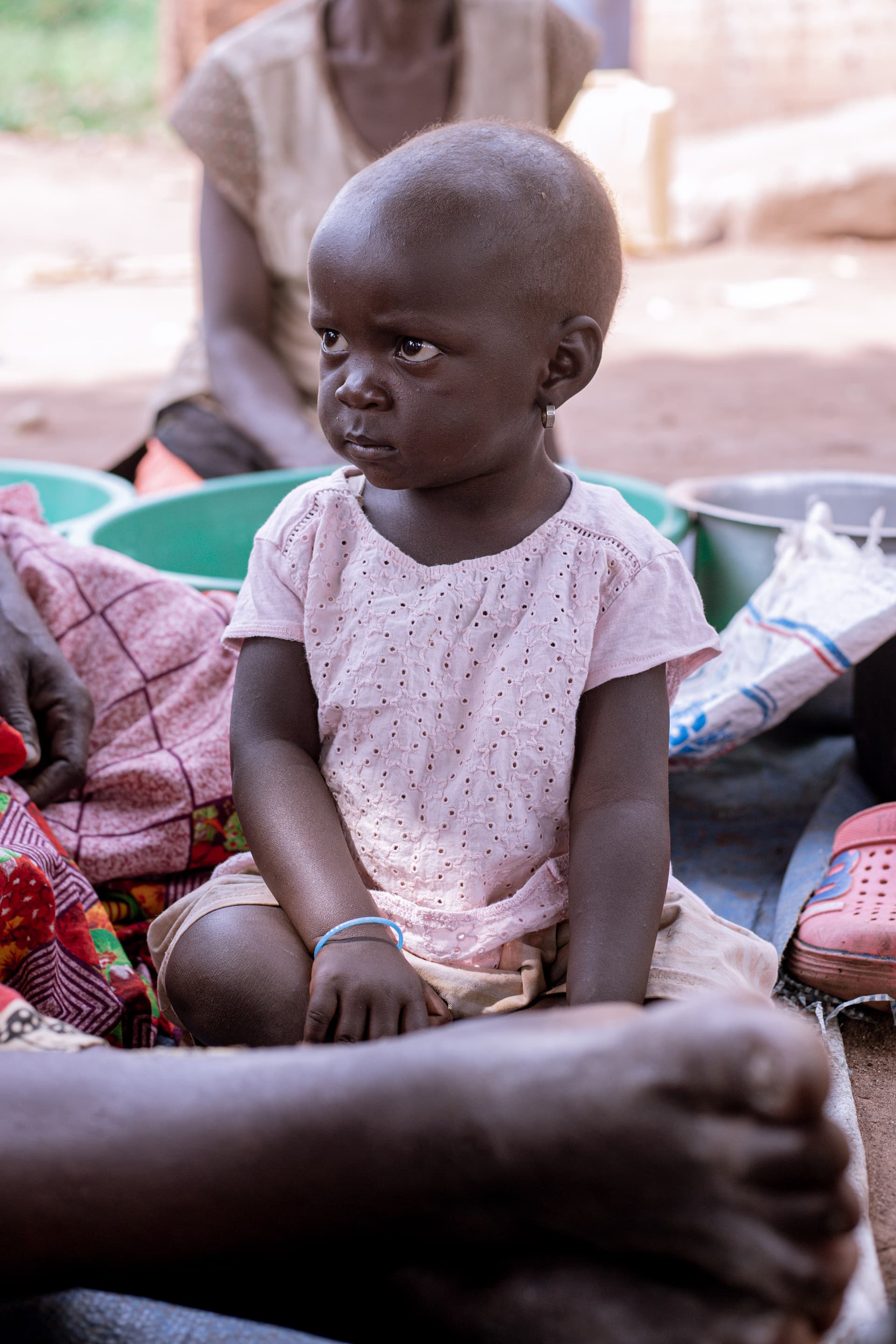 A young child sits among basins of clothing, looking at the camera.